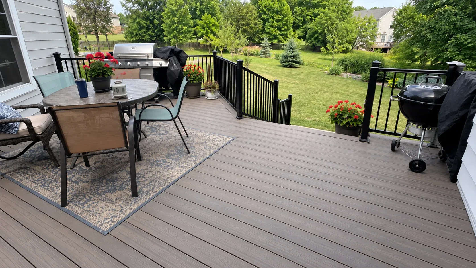 A composite deck against the house at golden hour, black aluminium railings and a short flight of steps down to the lawn